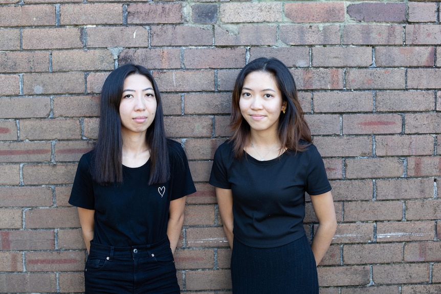 Two young women wearing black tshirts look seriously at the camera.