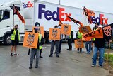 A group of men carrying placards in front of a big FedEx delivery truck