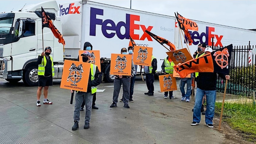 A group of men carrying placards in front of a big FedEx delivery truck