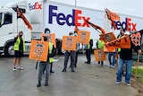A group of men carrying placards in front of a big FedEx delivery truck