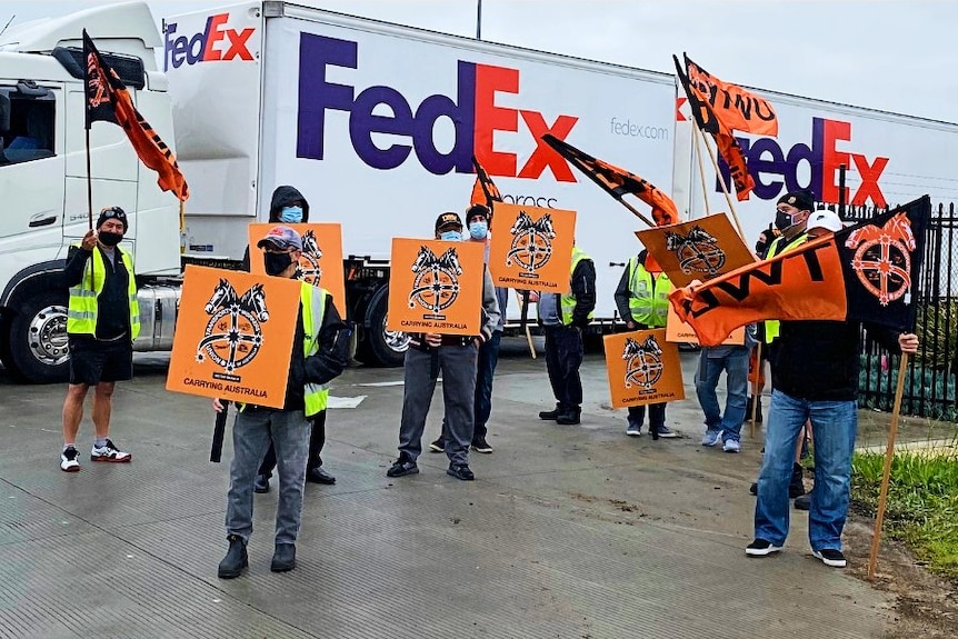 a group of men carrying placards in front of a big delivery truck