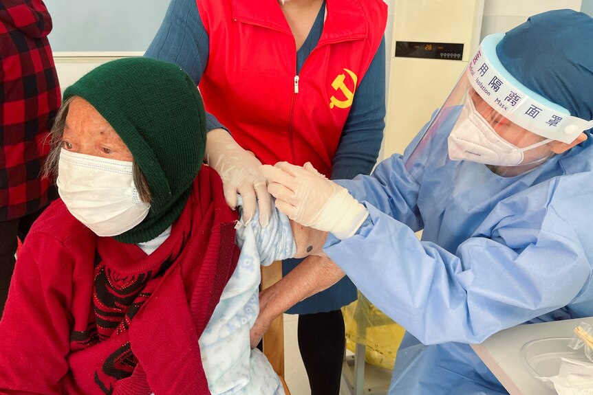 A medical worker administers a dose of a vaccine against COVID-19 to an elderly resident
