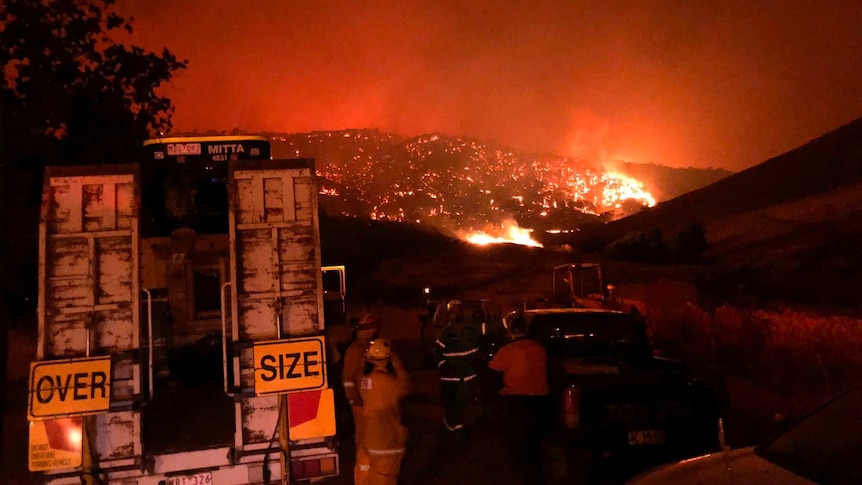 Firefighters gather in front of a mountain that is aglow with flames, near Corryong and Walwa.