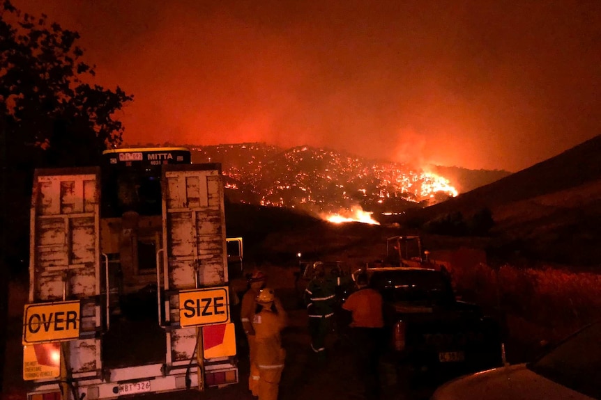 Firefighters gather in front of a mountain that is aglow with flames, near Corryong and Walwa.