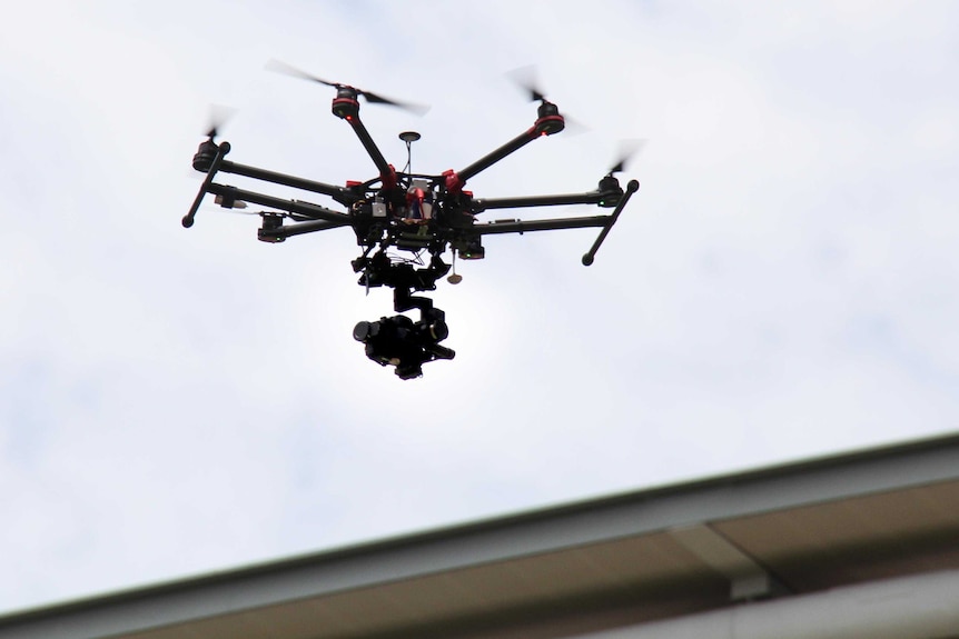 A drone in the air with the sky in the background and part of a building to the right.