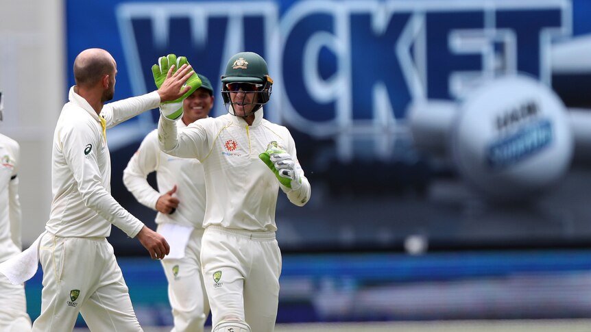 Two men high five with a blue sign in the background displaying the word, wicket