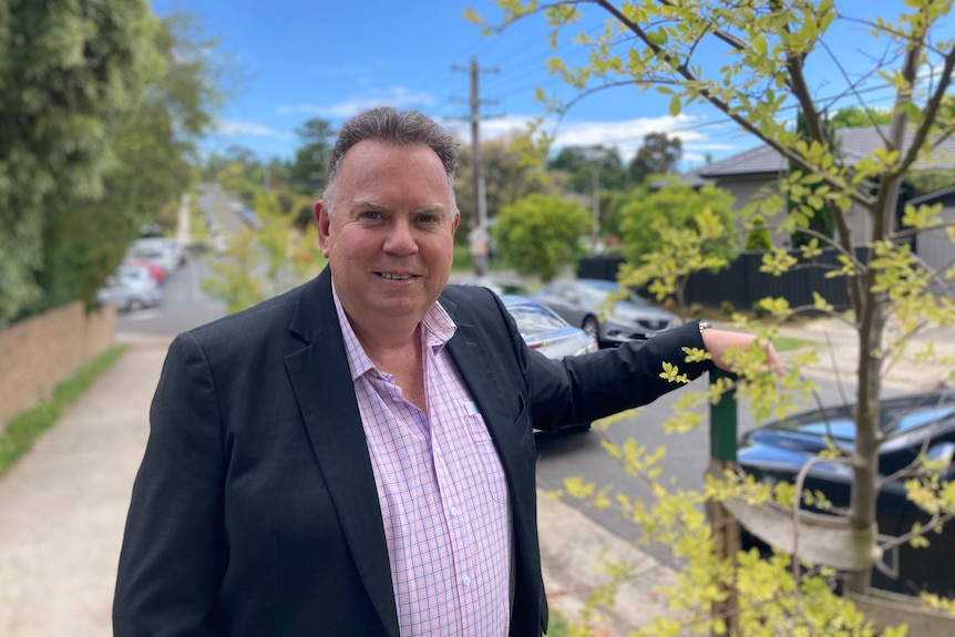 A man in a suit next to a tree on the side of the street.