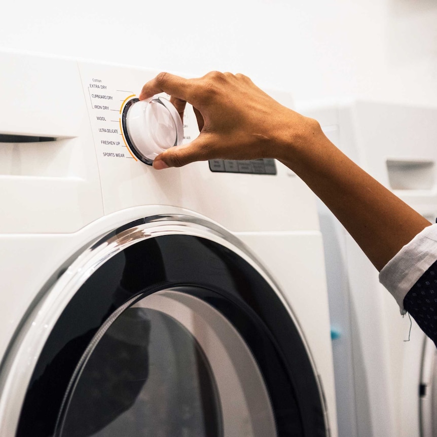 A woman's hand adjusts a dial on a washing machine