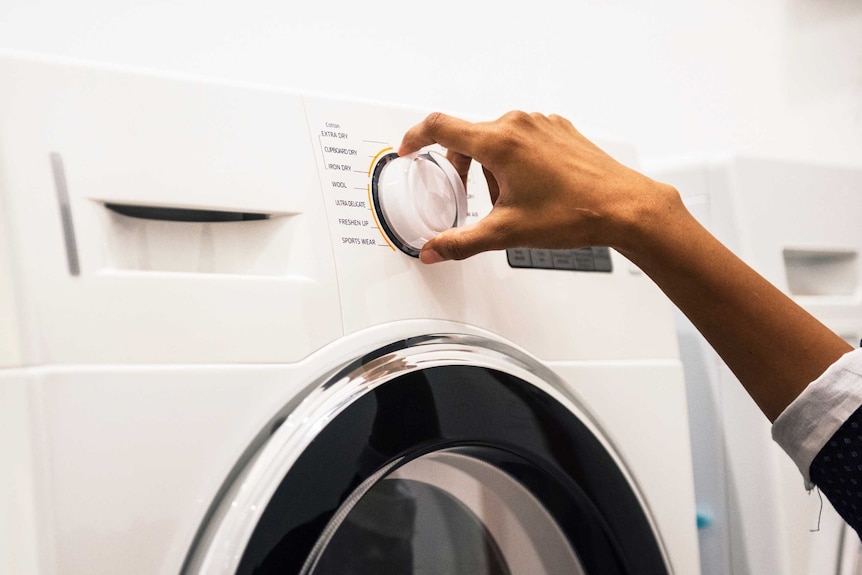 A woman's hand adjusts a dial on a washing machine