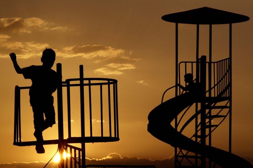 Children play in a playground as the sun sets