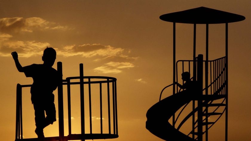 Children play in a playground as the sun sets