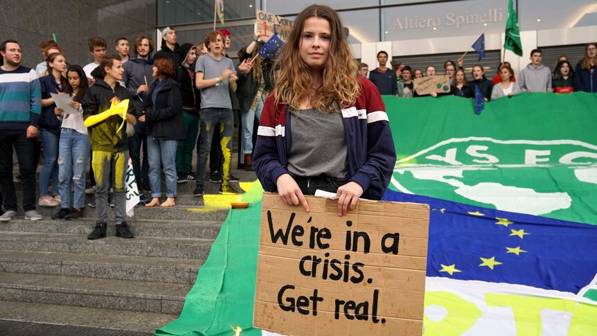 Luisa Neubauer, standing in front of other activists, holds a sign saying "We're in a crisis. Get real".