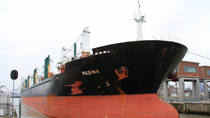 A large shipping vessel called Regina pulling into a port.