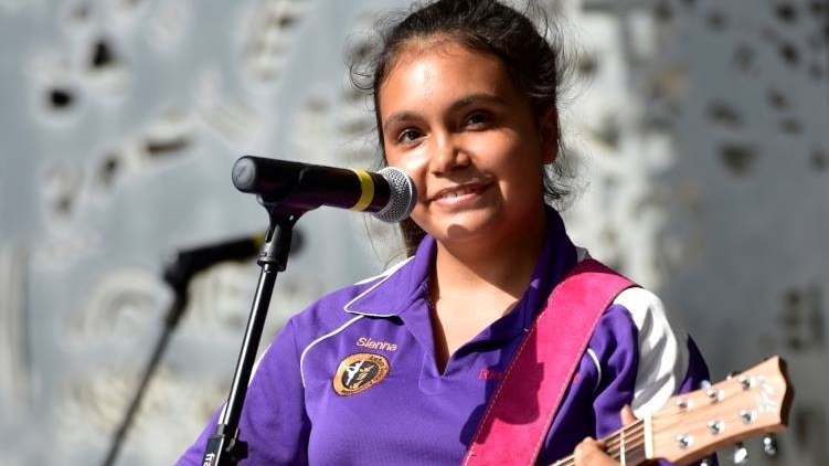 A young Indigenous woman plays a guitar.