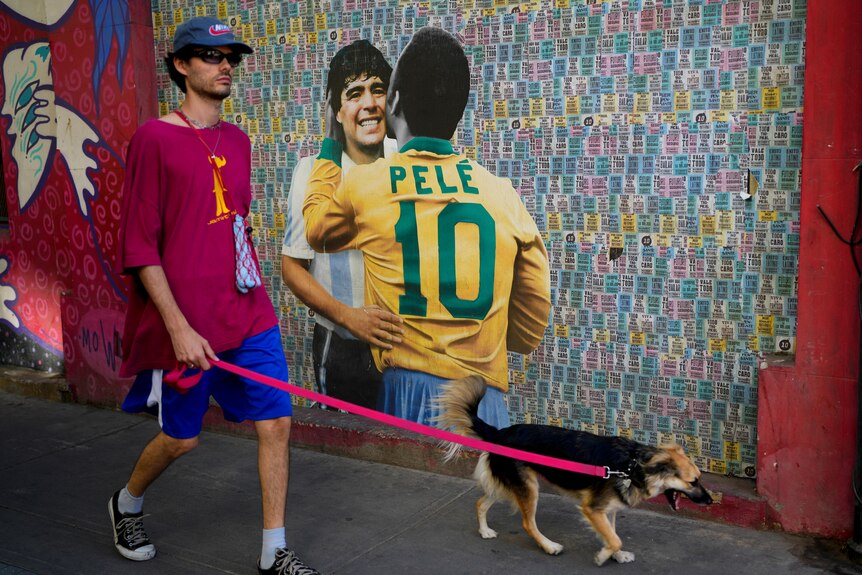 A man walks his dog past a mural showing Brazilian soccer legend Pele and Argentina late soccer star Diego Maradona