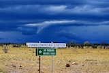 Dark storm clouds over Thargomindah Station with road signs in the foreground