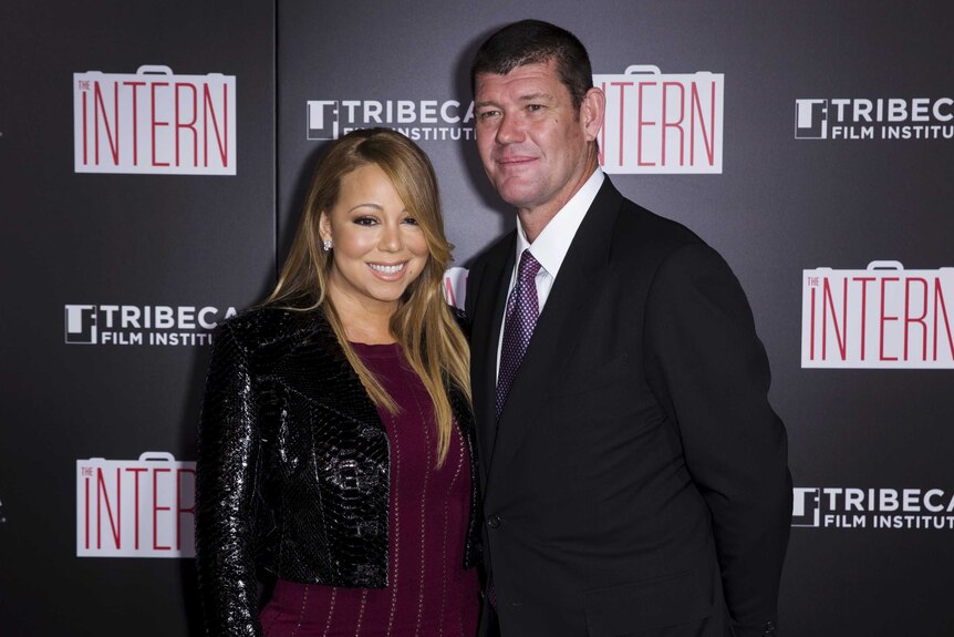 Mariah Carey smiles next to James Packer in front of a wall with advertisements for the move The Intern.