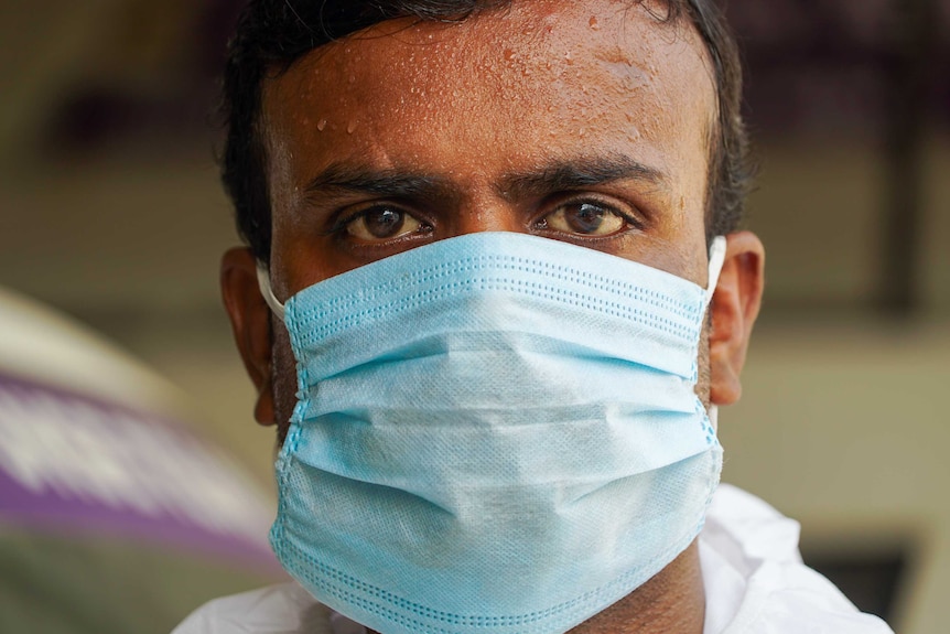 A young Indian man in a face mask with a sweaty forehead