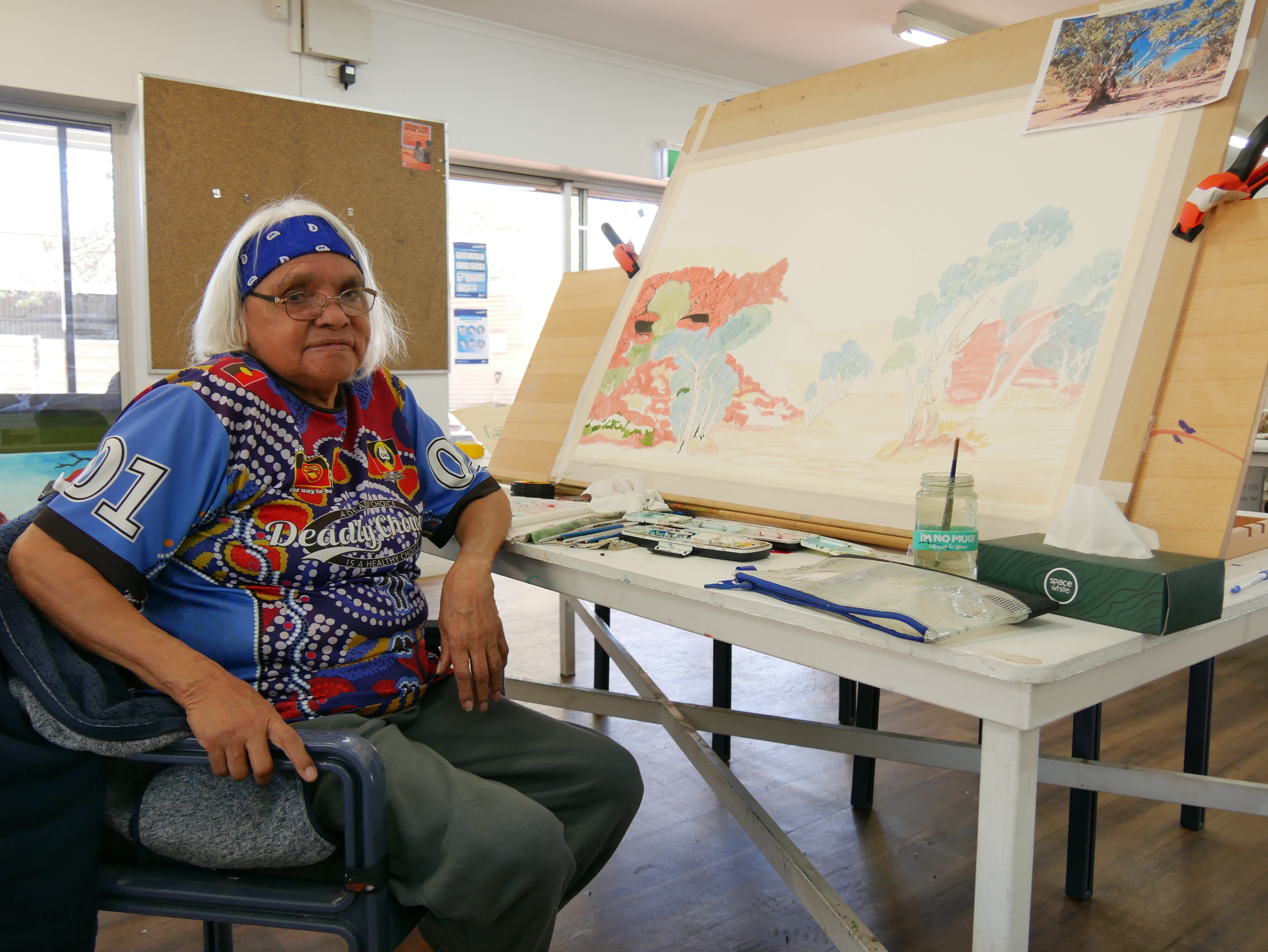 A woman sits beside her watercolor painting in progress