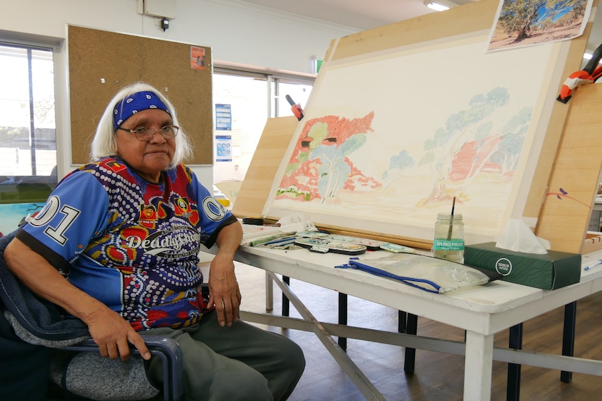 A woman sits beside her watercolour painting in progress