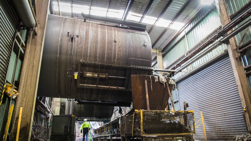 A large metal cylinder hangs over a conveyor belt.