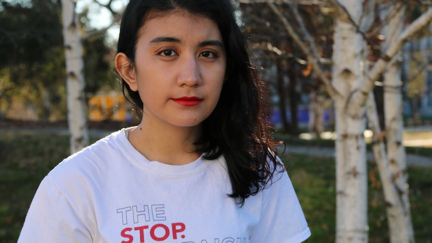 Mina Khoshnevisan looks serious while sitting outside at the ANU, trees behind her.