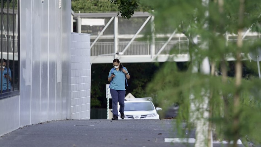 Woman with white mask walks while looking at her phone in an empty street.