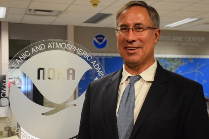 Chris Landsea standing in front of a NOAA logo.