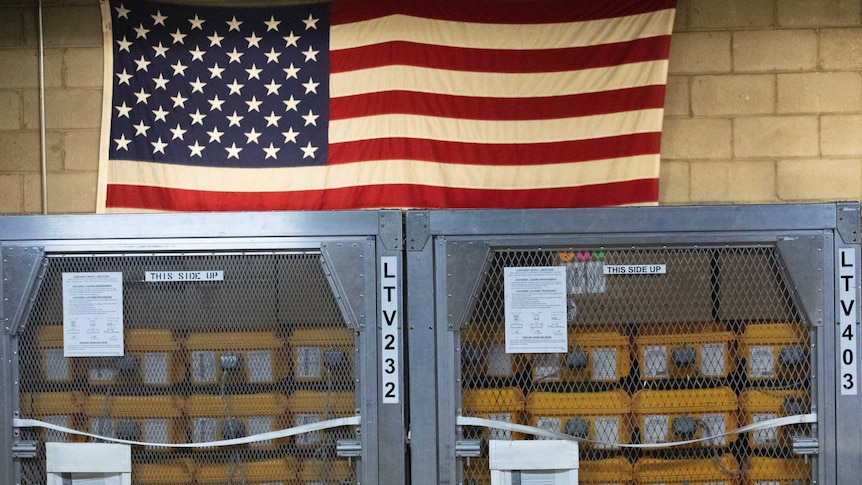 Cages of ventilators, part of a shipment of 400, are displayed in front of an American flag.