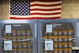 Cages of ventilators, part of a shipment of 400, are displayed in front of an American flag.