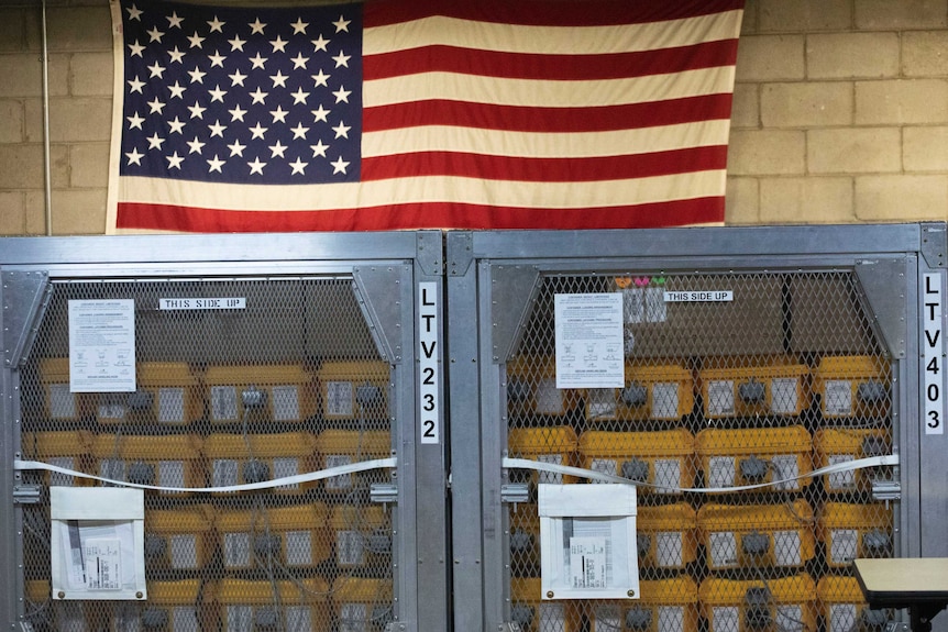 Cages of ventilators, part of a shipment of 400, are displayed in front of an American flag.
