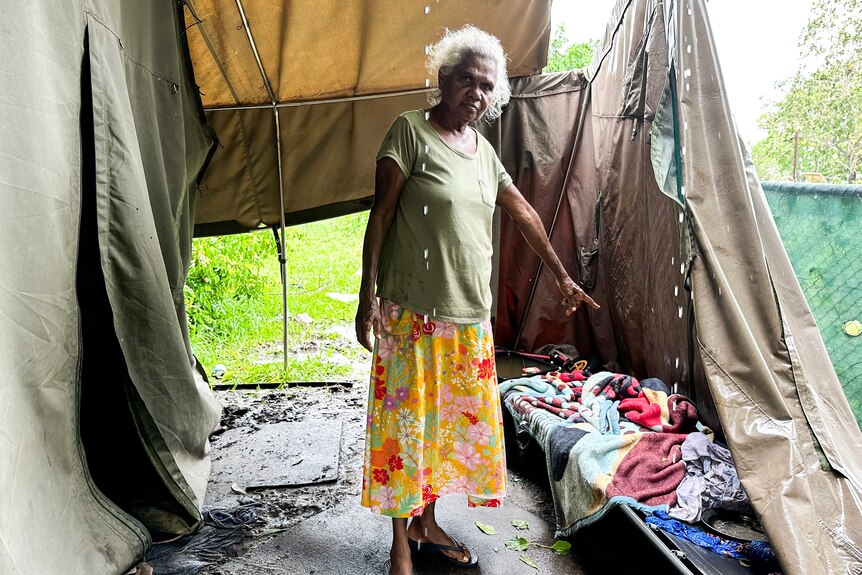 A woman stands inside a damaged tent. 