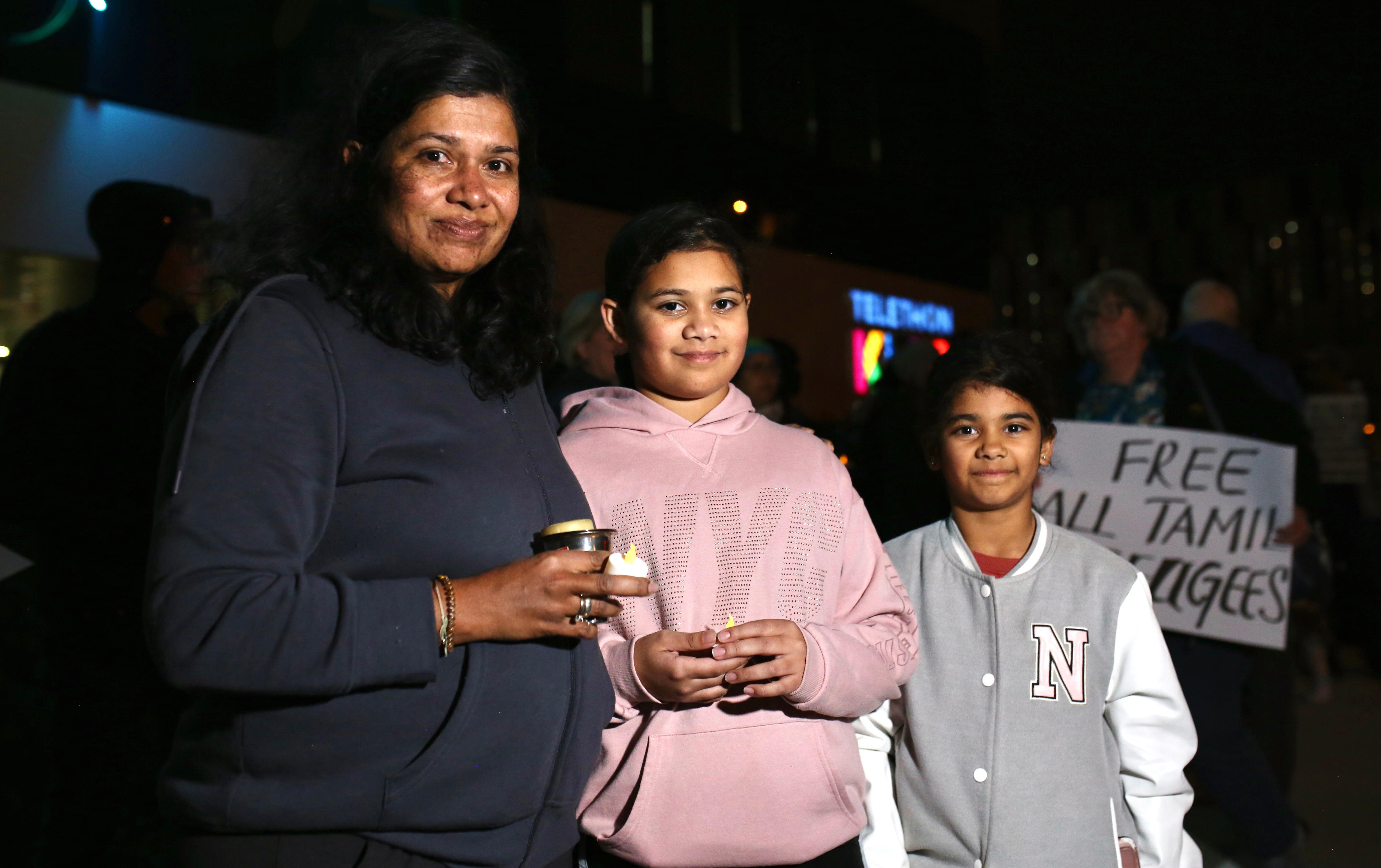 A mother and her daughters hold candles in the dark outside a hospital.