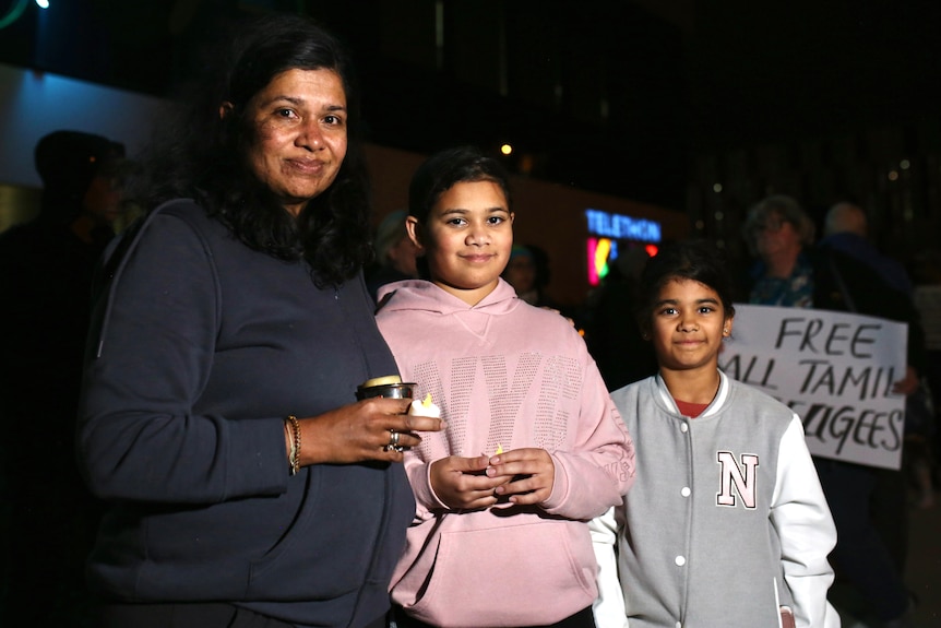 A mother and her daughters hold candles in the dark outside a hospital.