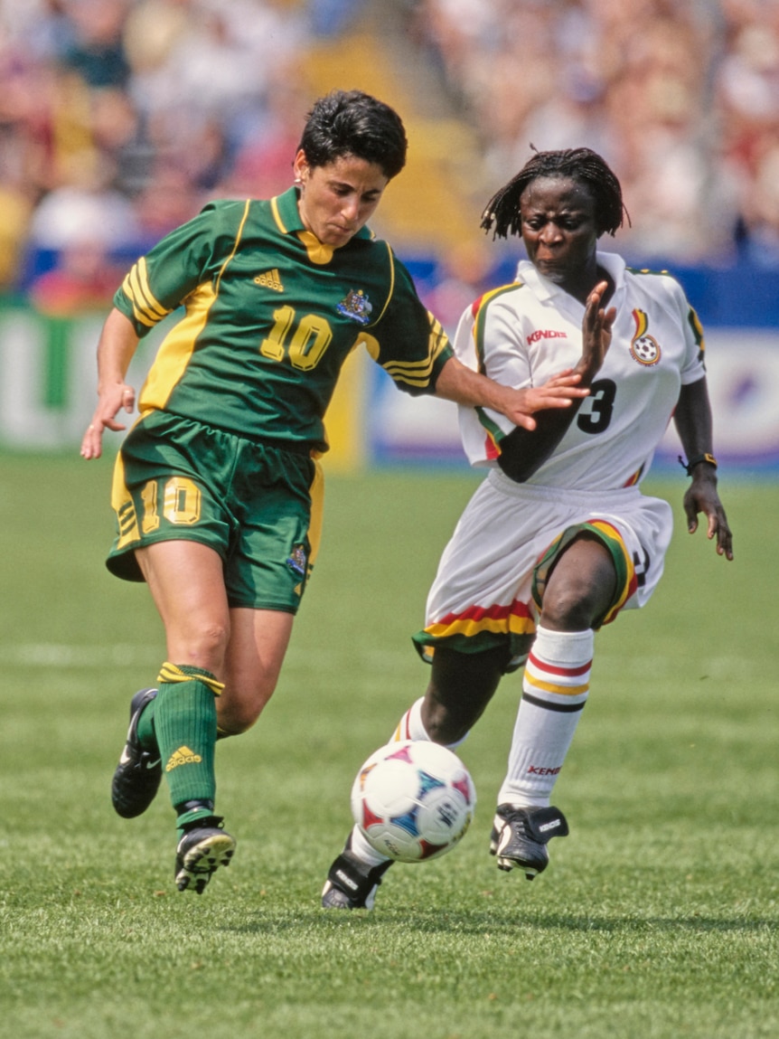 Two soccer players, one wearing green and yellow and the other wearing white, run for the ball during a game
