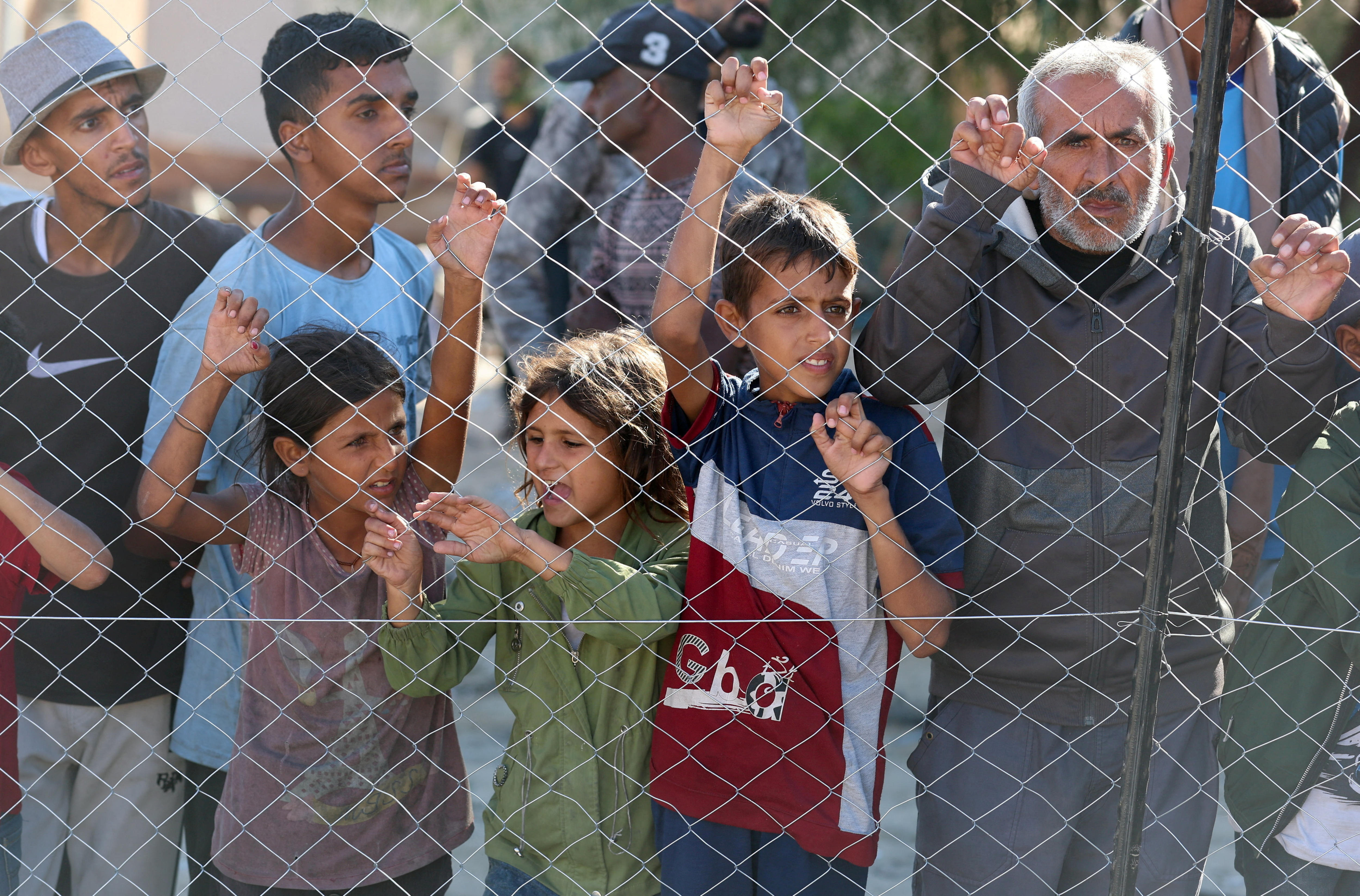 People stand at a wire-lined fence watching as a truck passes by.