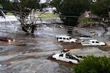 Cars in brown floodwaters with sign for Northam Agricultural Society in the background.