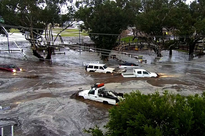 Cars in brown floodwaters with sign for Northam Agricultural Society in the background.