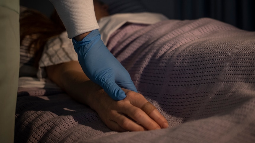 A gloved hand resting on a girl's hand in a hospital 