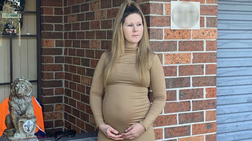 pregnant woman holding her stomach outside a house