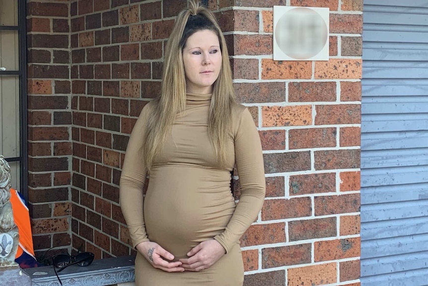 pregnant woman holding her stomach outside a house