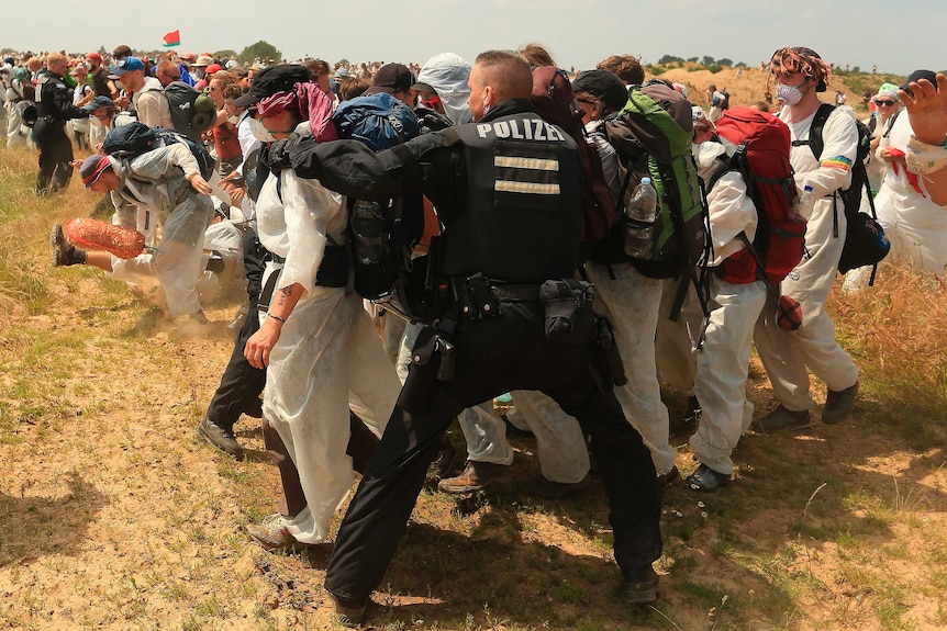 Activists clash with police on an open dry field.