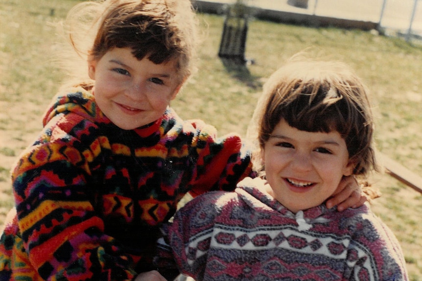 Twin sisters as young children with their arms around each other