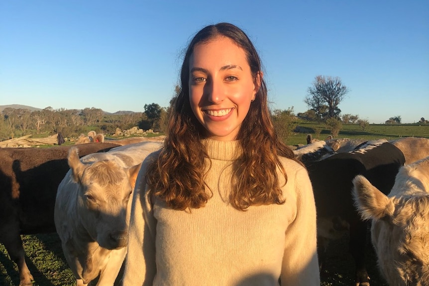 Young womanl standing in a paddock surrounded by cows.