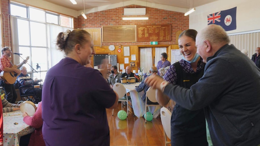 Aged care staff dancing and laughing with elderly people to a live guitarist.