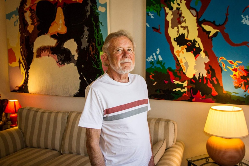 Derek Maitland standing in front of some of his paintings.