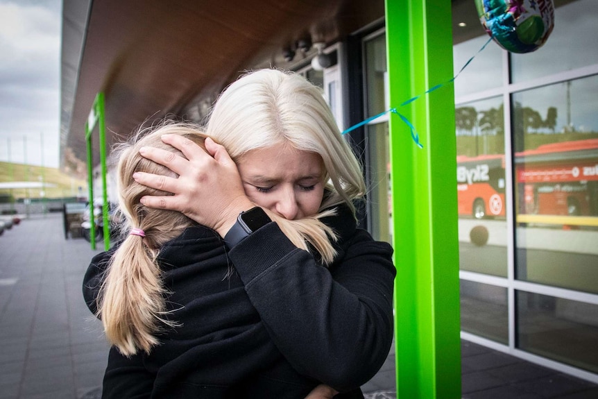 Woman embraces young girl.