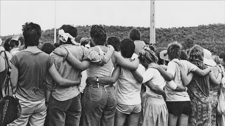 Protesters stand linked together at the Pine Gap Women's Peace Camp in 1983, photo taken from behind, bushland in background