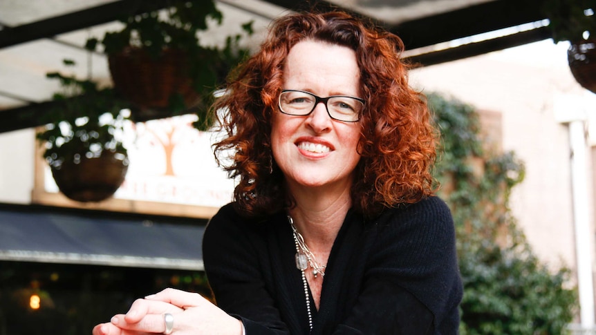 A portrait of Professor Genevieve Bell, smiling and sitting in a leafy cafe.