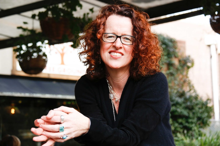 A portrait of Professor Genevieve Bell, smiling and sitting in a leafy cafe.